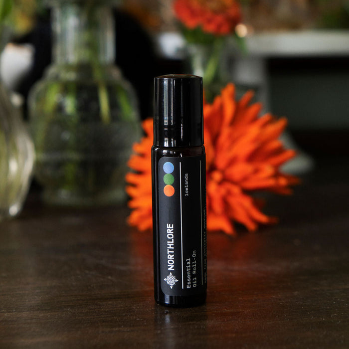 Black Northland essential oil roller bottle on a wooden surface with flowers in the background